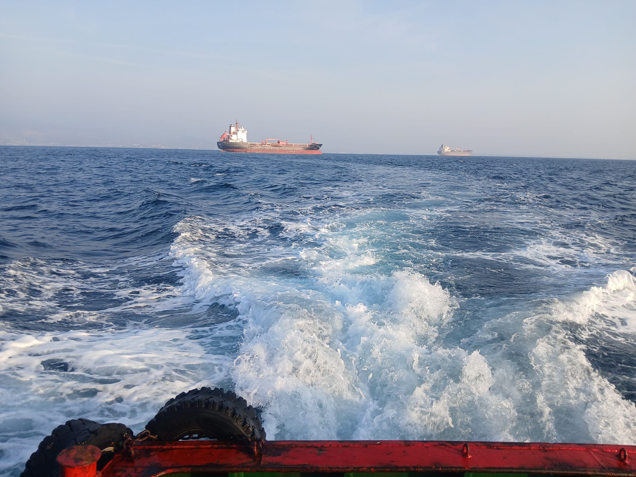 View across a boat wake towards tankers at sea